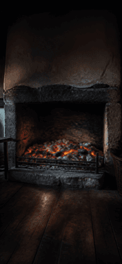 Glowing logs and embers sit inside a dark stone cottage fireplace.
